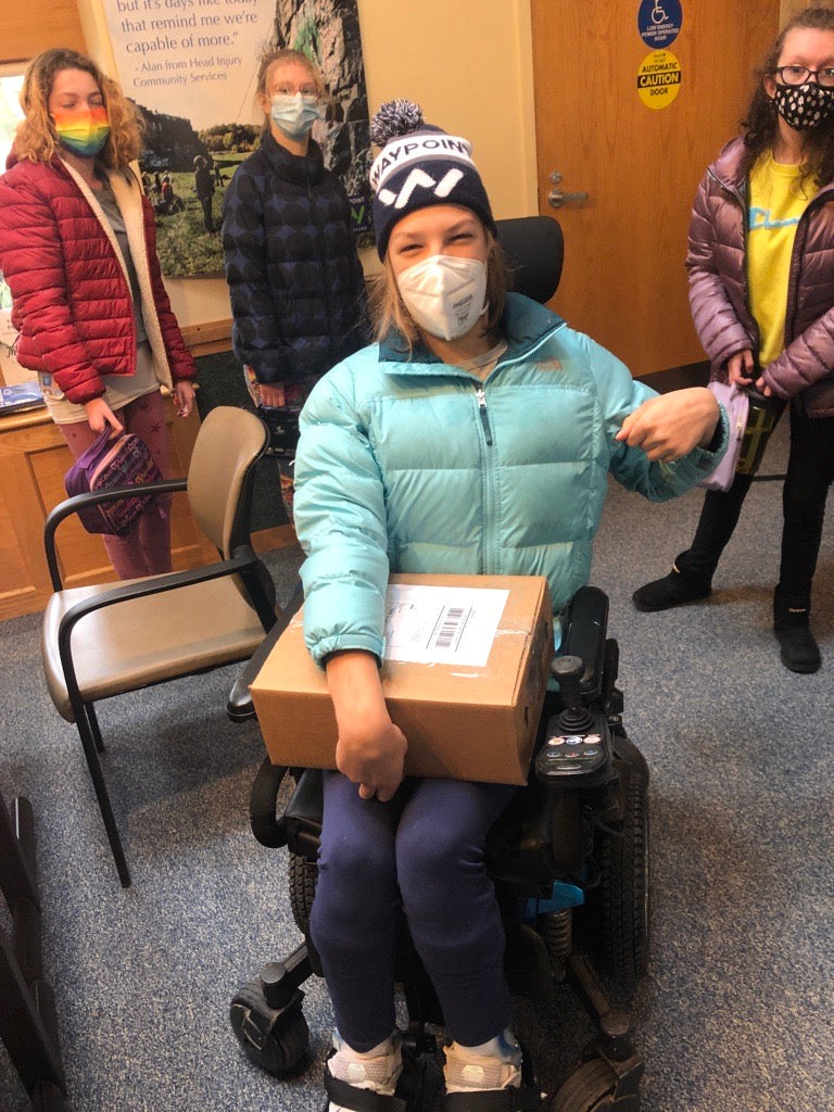 A high school student using a wheelchair wearing a Waypoint winter beanie and holding a cardboard box package with label to be mailed out to a customer